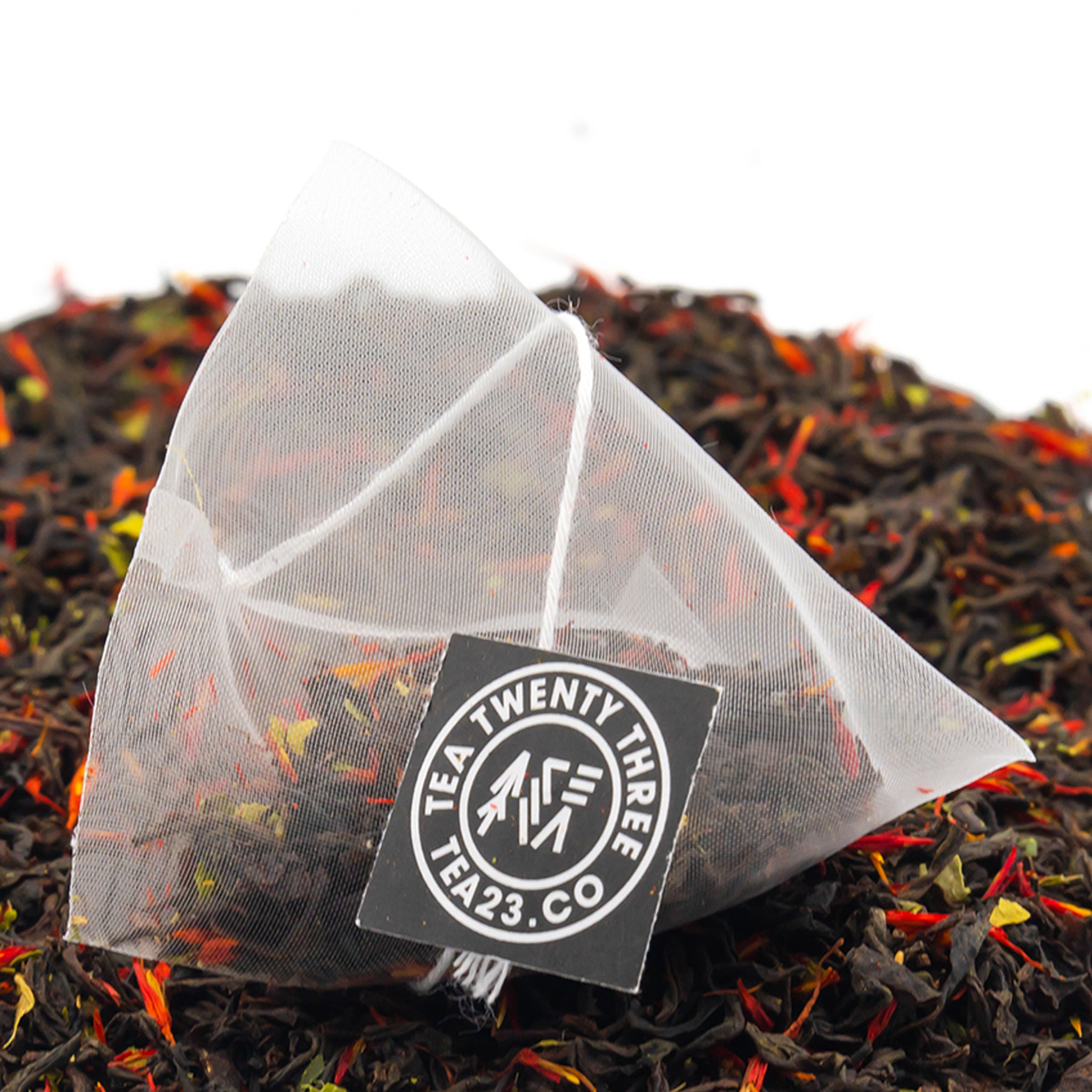 An Earl Grey pyramid tea bag sits on a pile of loose Earl grey tea. Shop the range of TEA23 tea bag teas and infusion.