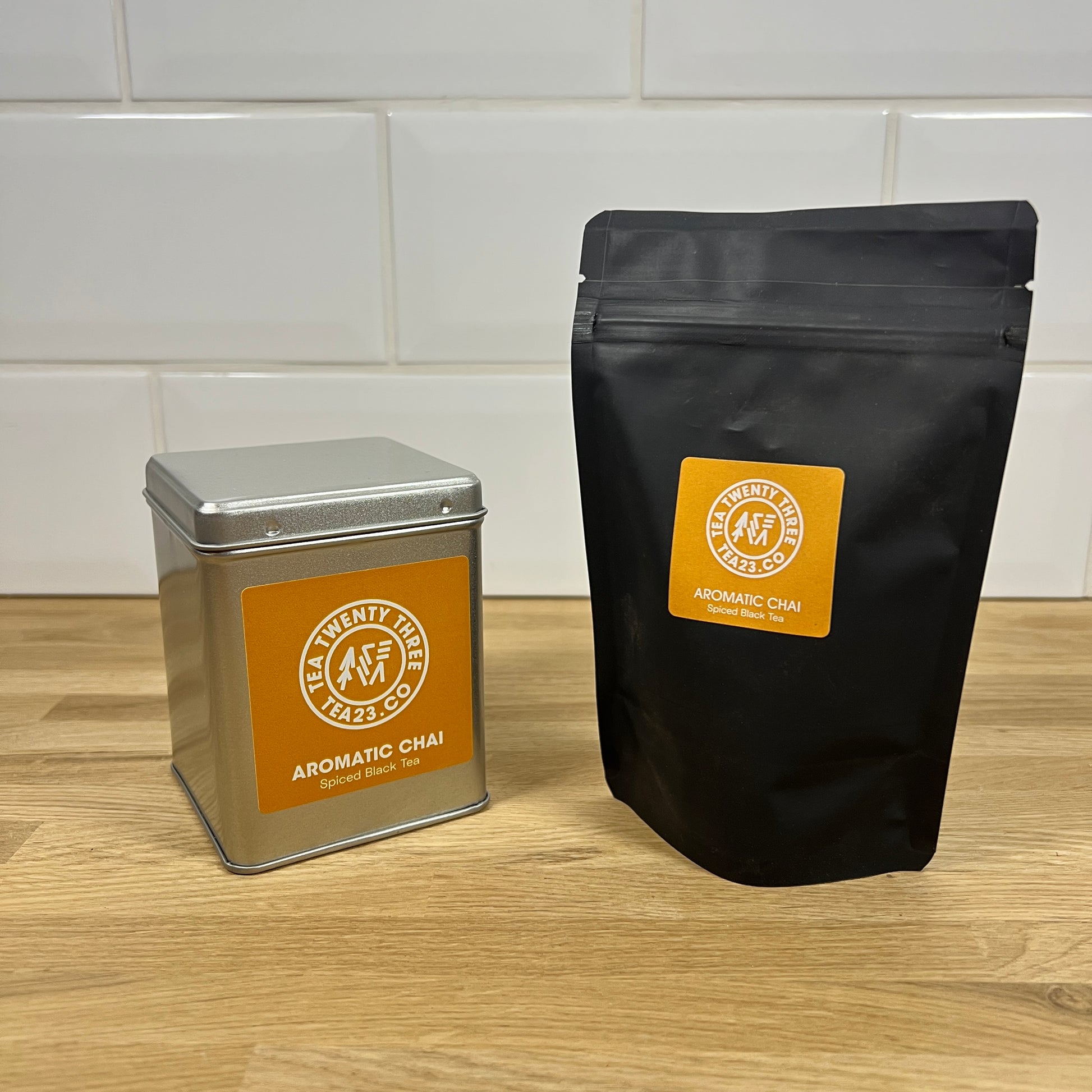 Tea packaging including a metal canister and black bag with a visible brand logo on a wooden surface.