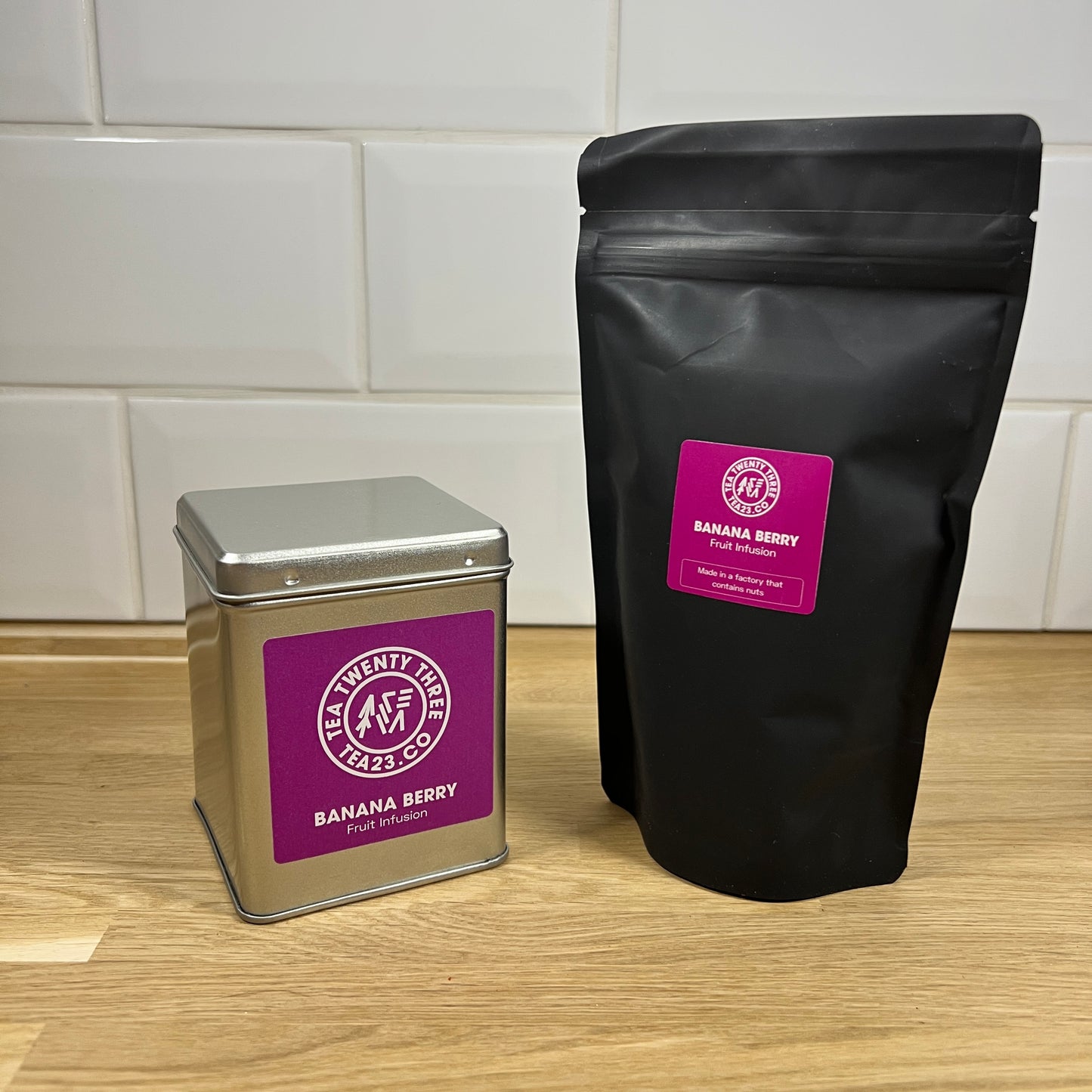 A silver gift tin and black pouch of Banana Berry fruit tea