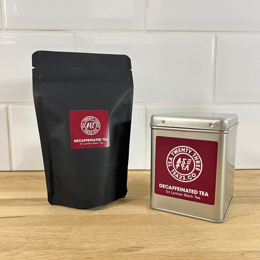 Black tea bag and silver tea canister with red burgundy label on a wooden surface.