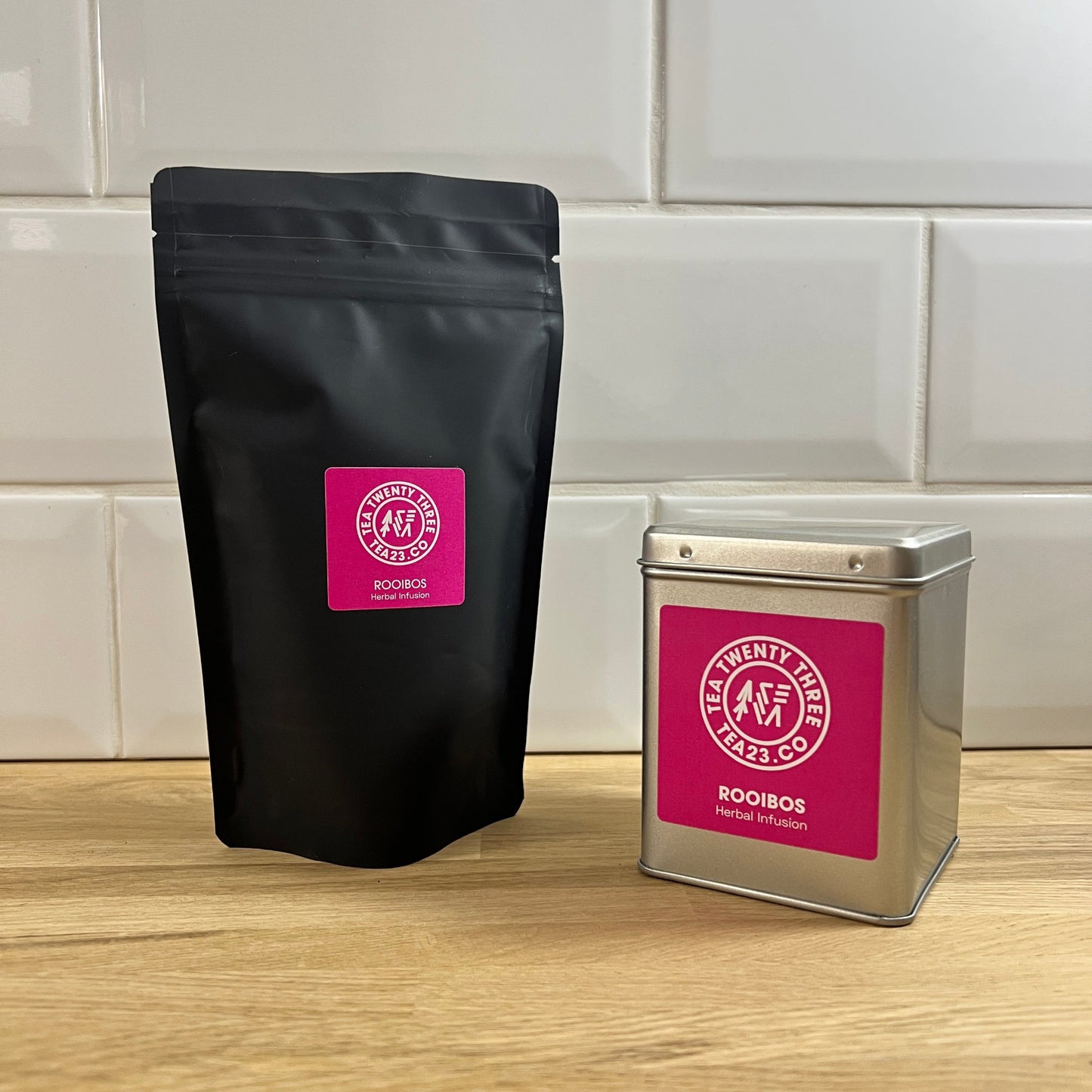 Black tea bag and silver tin with a pink label on a wooden surface.