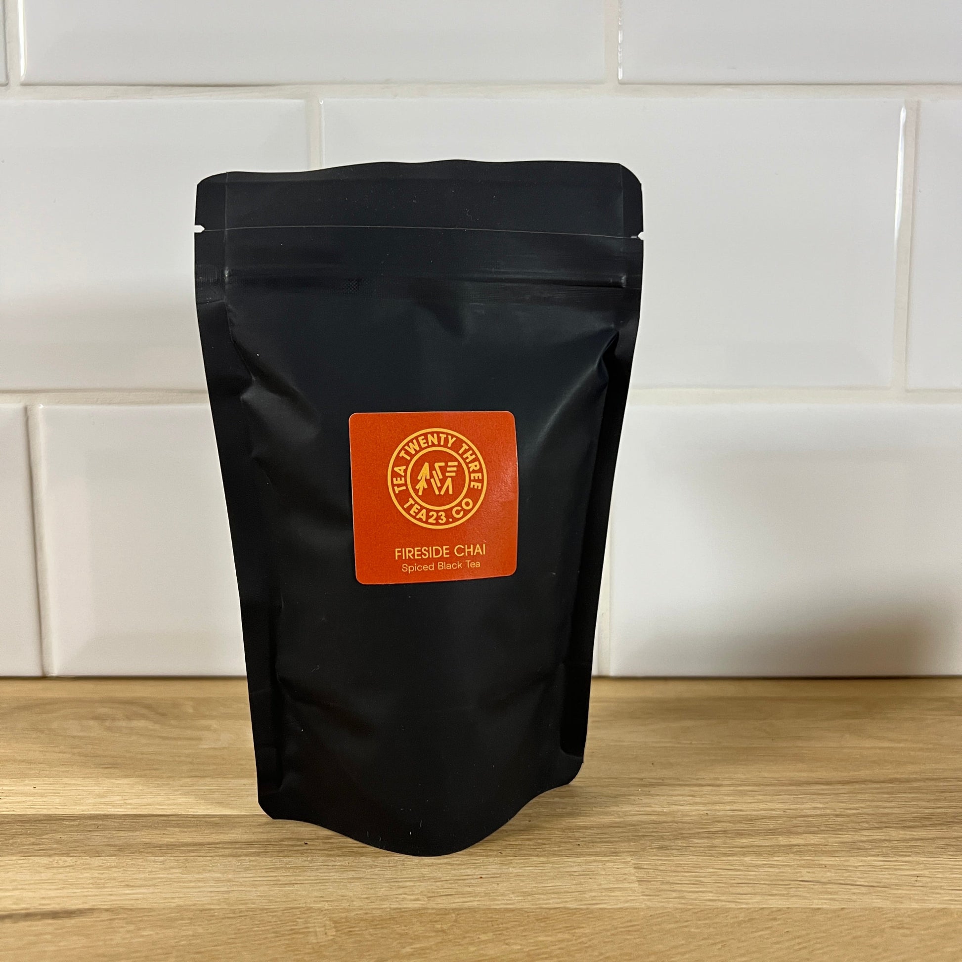 Black tea package with orange label on a wooden surface and white tiled wall background