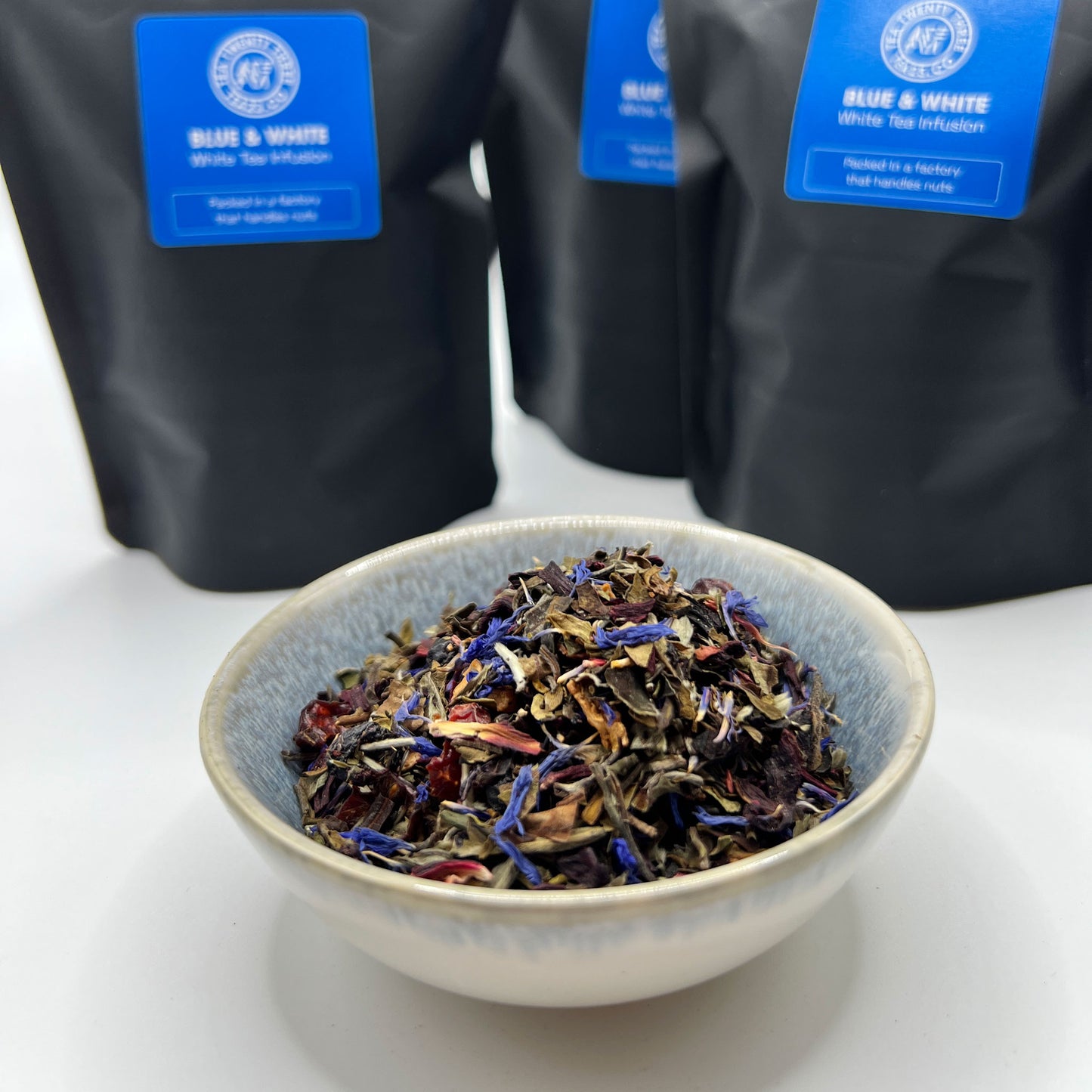 Tea leaves in a bowl with black tea bags labeled 'Blue & White' in the background.