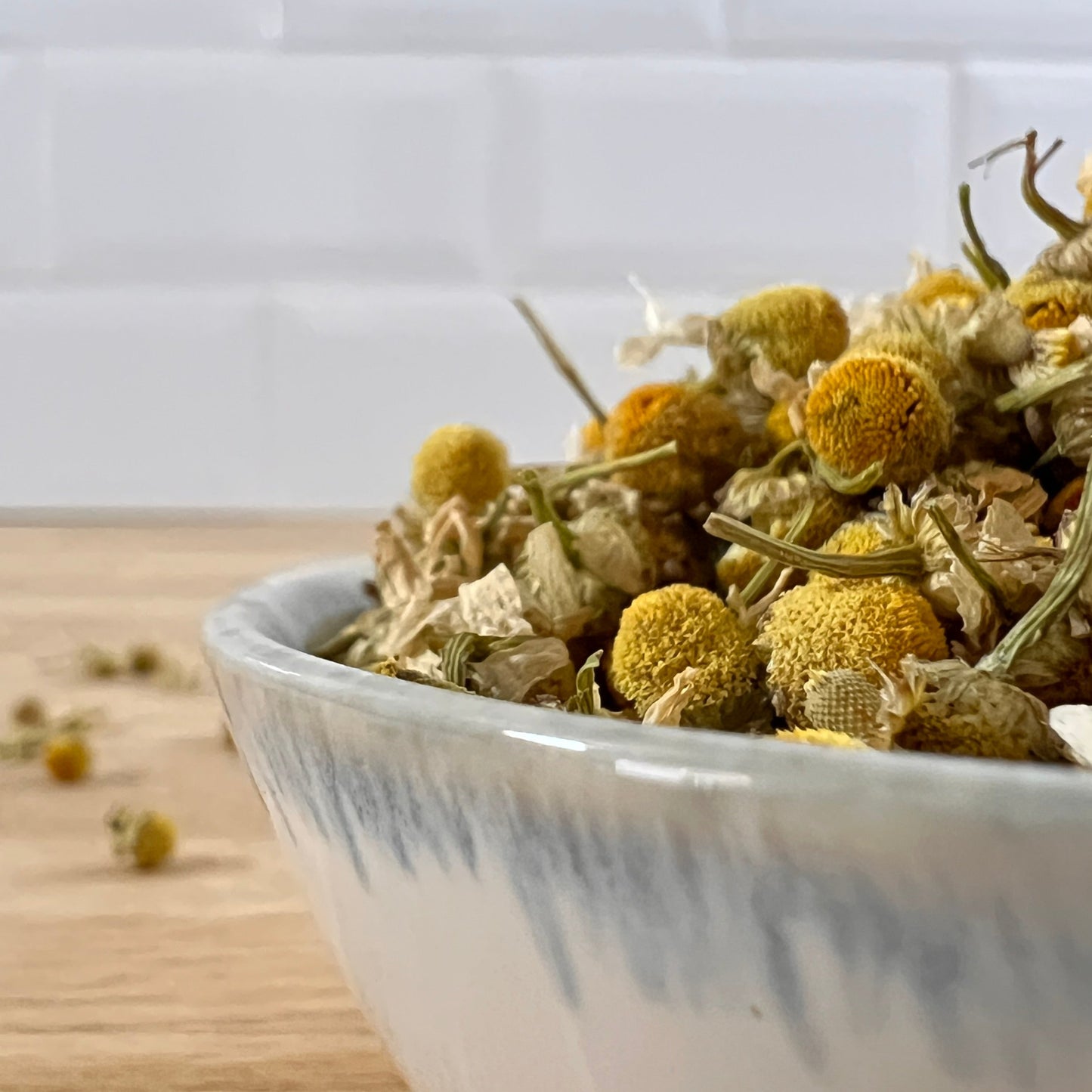 White bowl filled with dried chamomile flowers on a wooden surface.