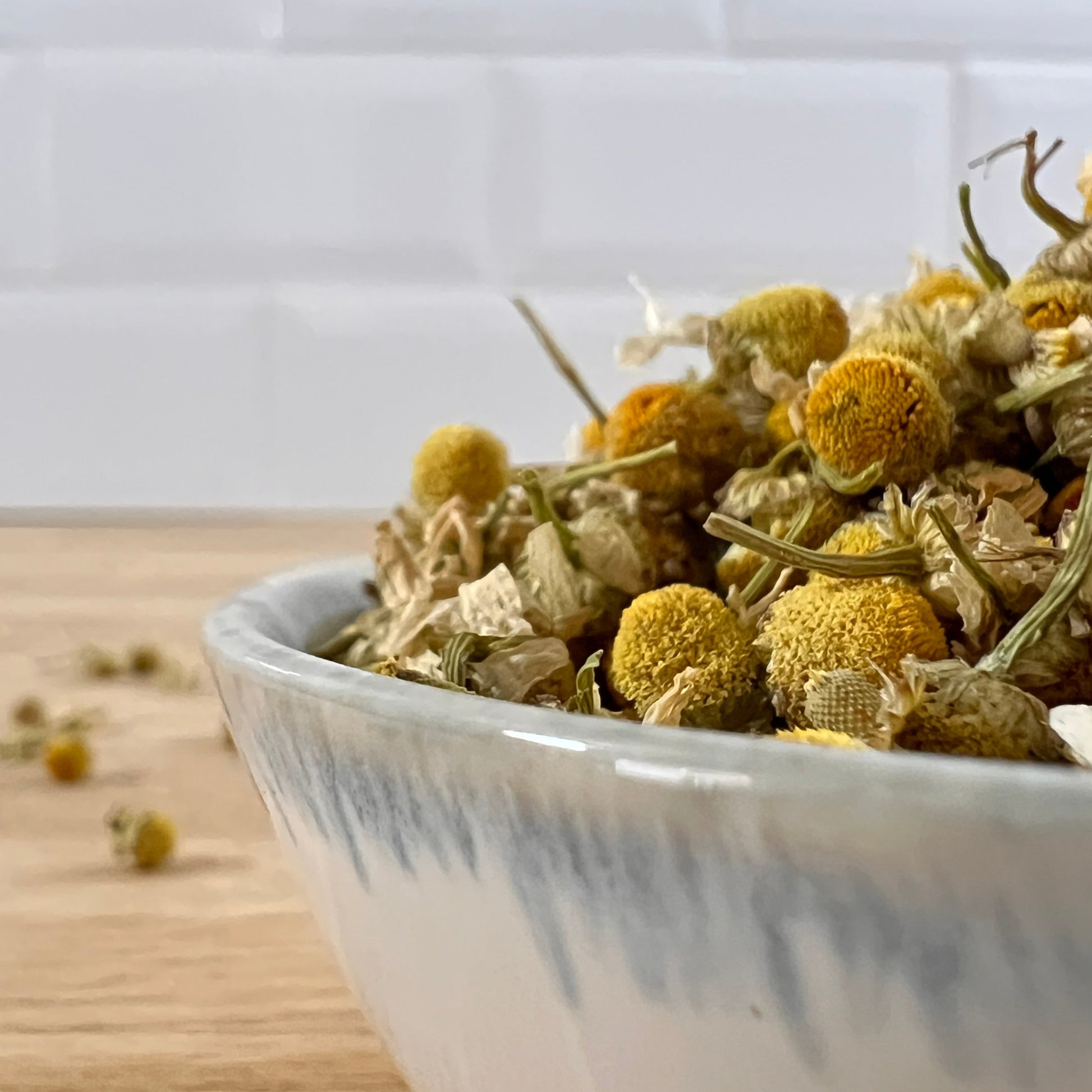 White bowl filled with dried chamomile flowers on a wooden surface.