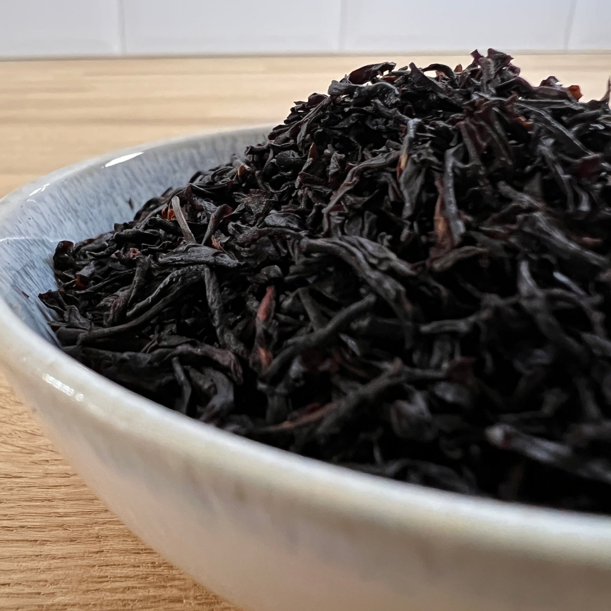 Close up of black tea leaves in a white dish on a wooden table