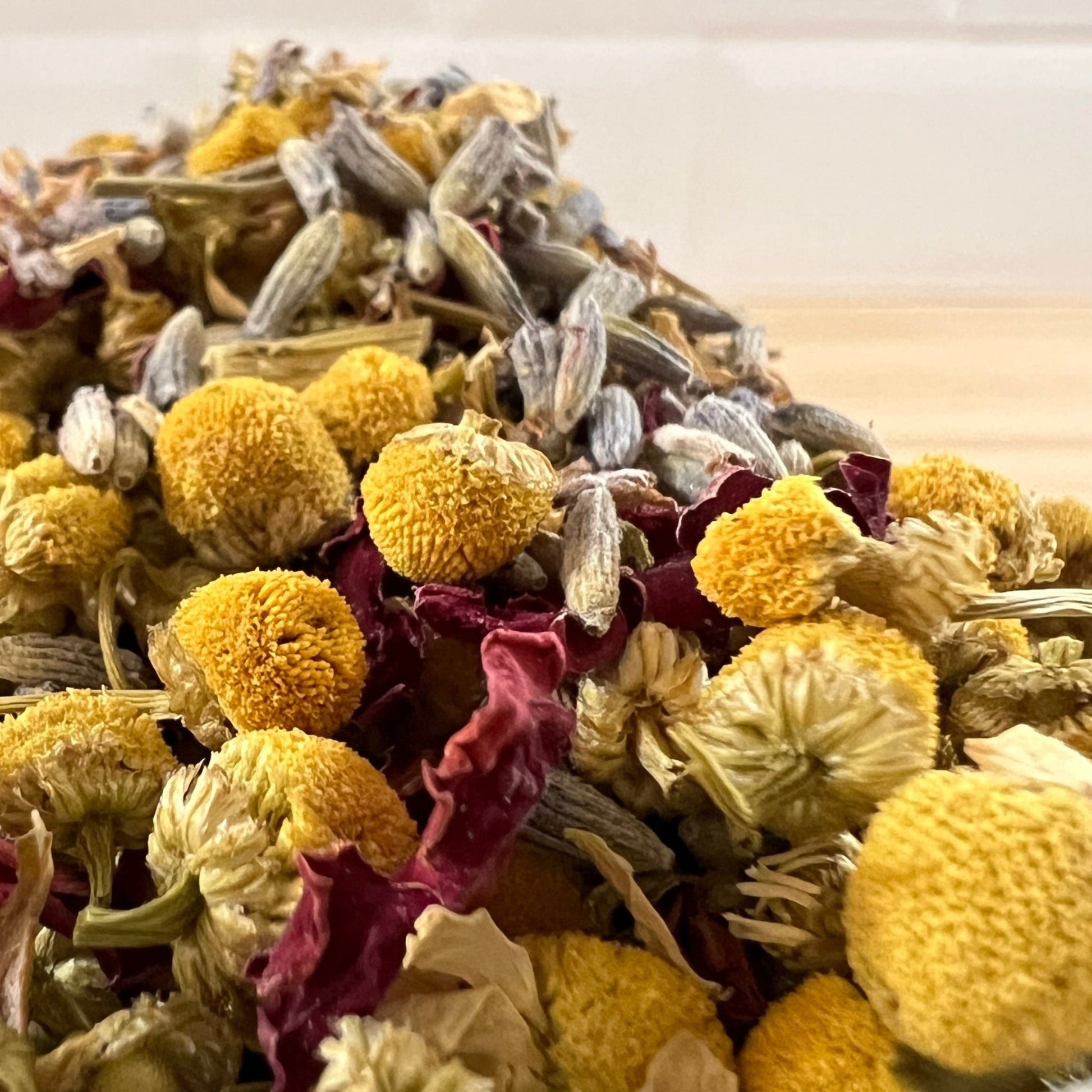Bowl filled with a mix of chamomile, lavender, rose petals on a wooden surface.