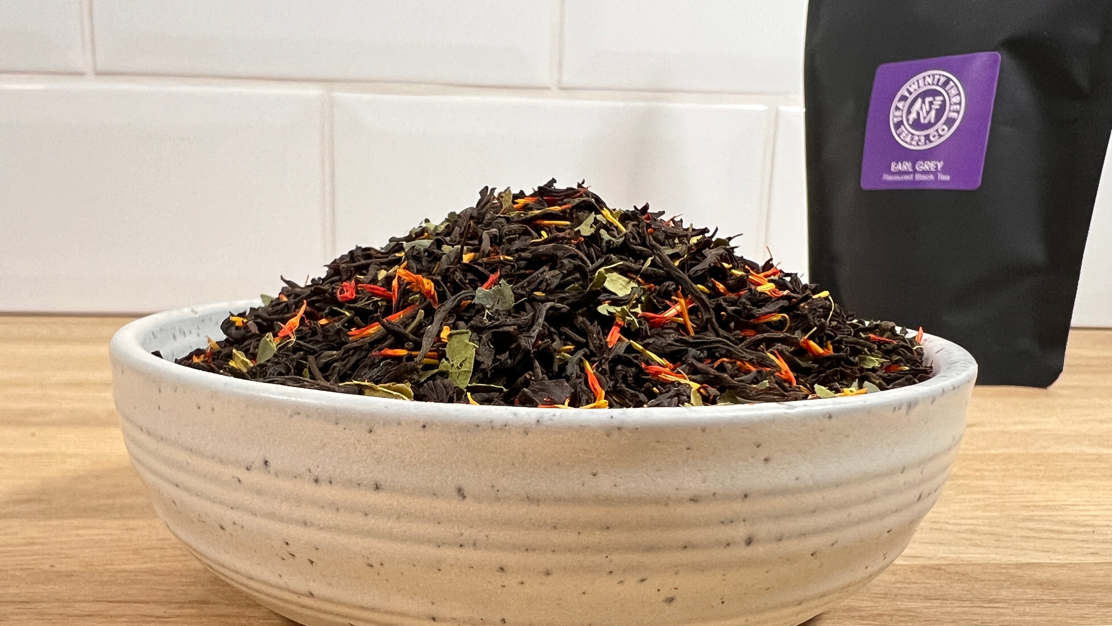 Tea leaves in a bowl with a bag of Earl Grey tea in the background.