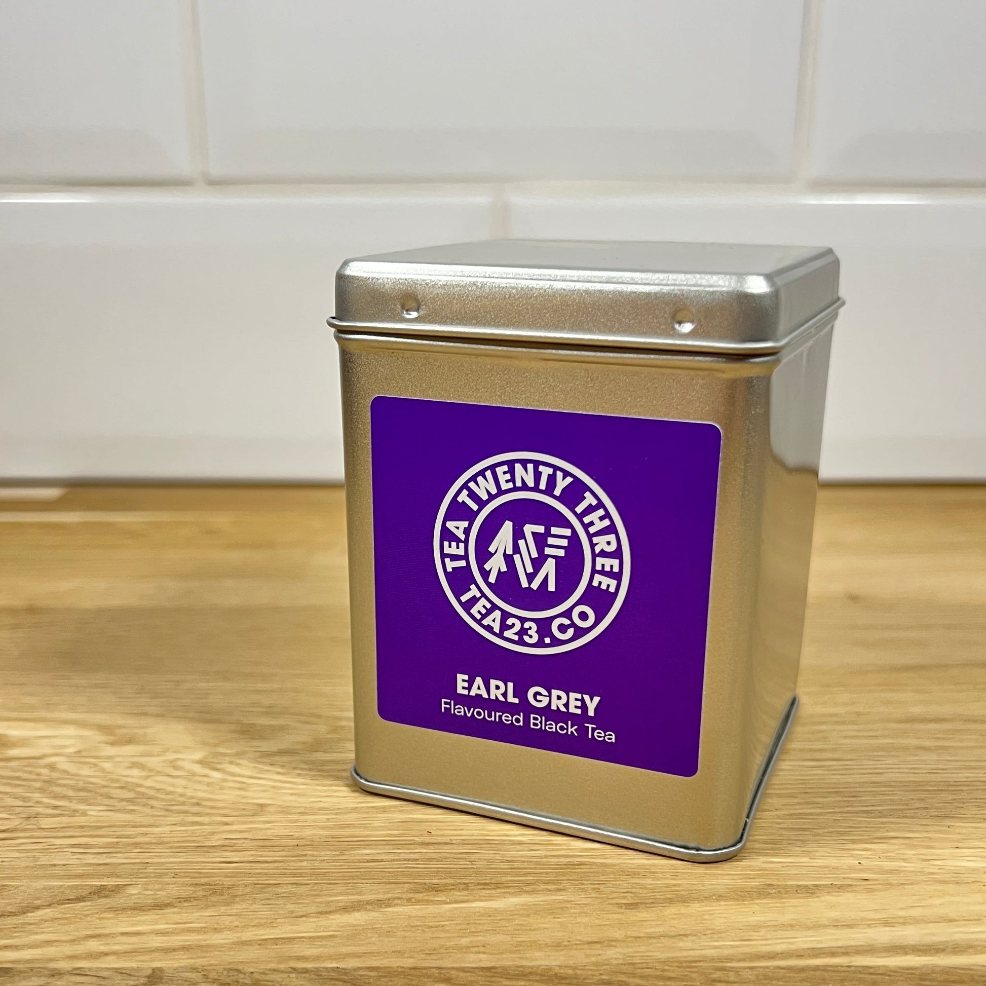 A silver tea tin of Earl Grey tea with a purple label on a wooden surface