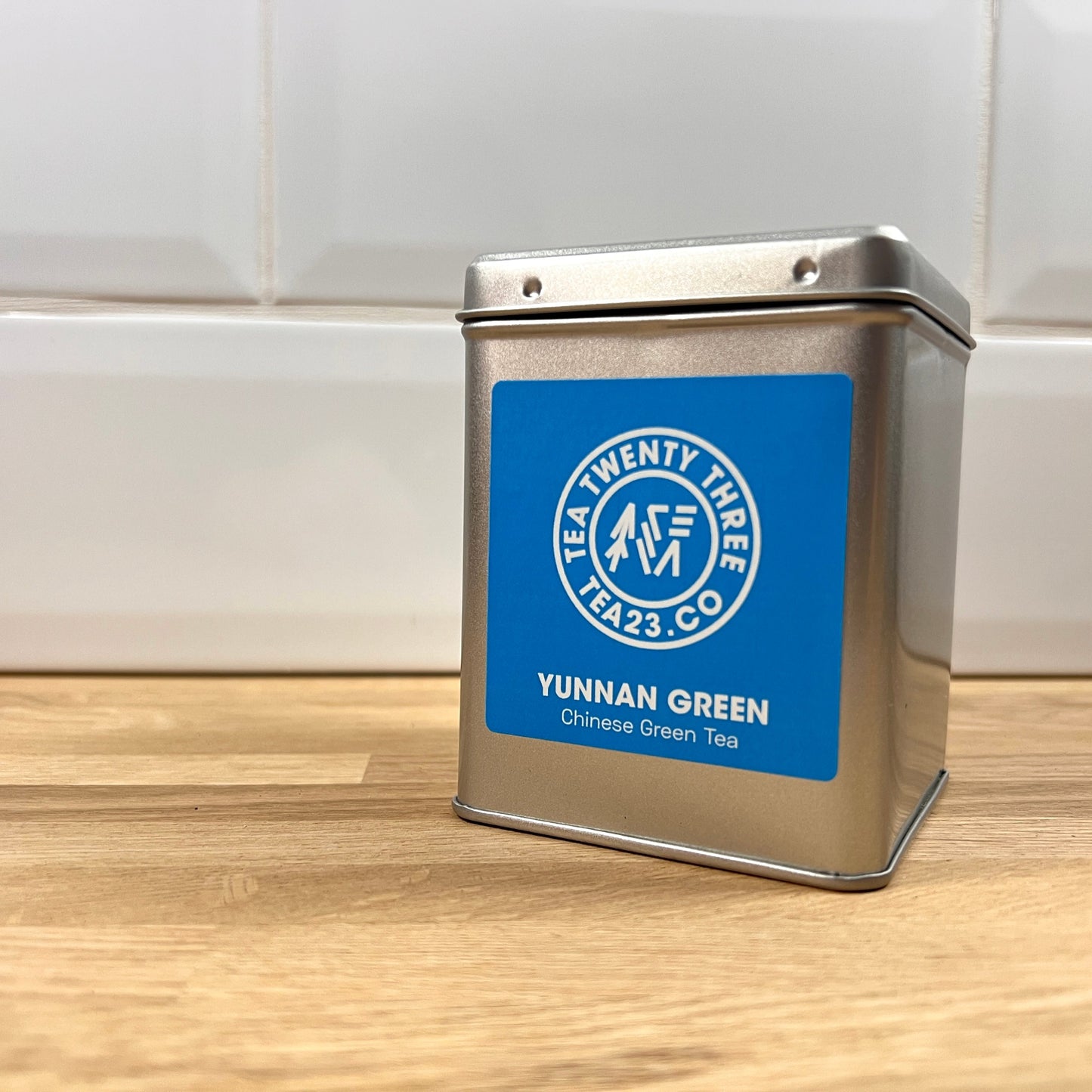 A silver tin with a blue label on a table with white tiles behind