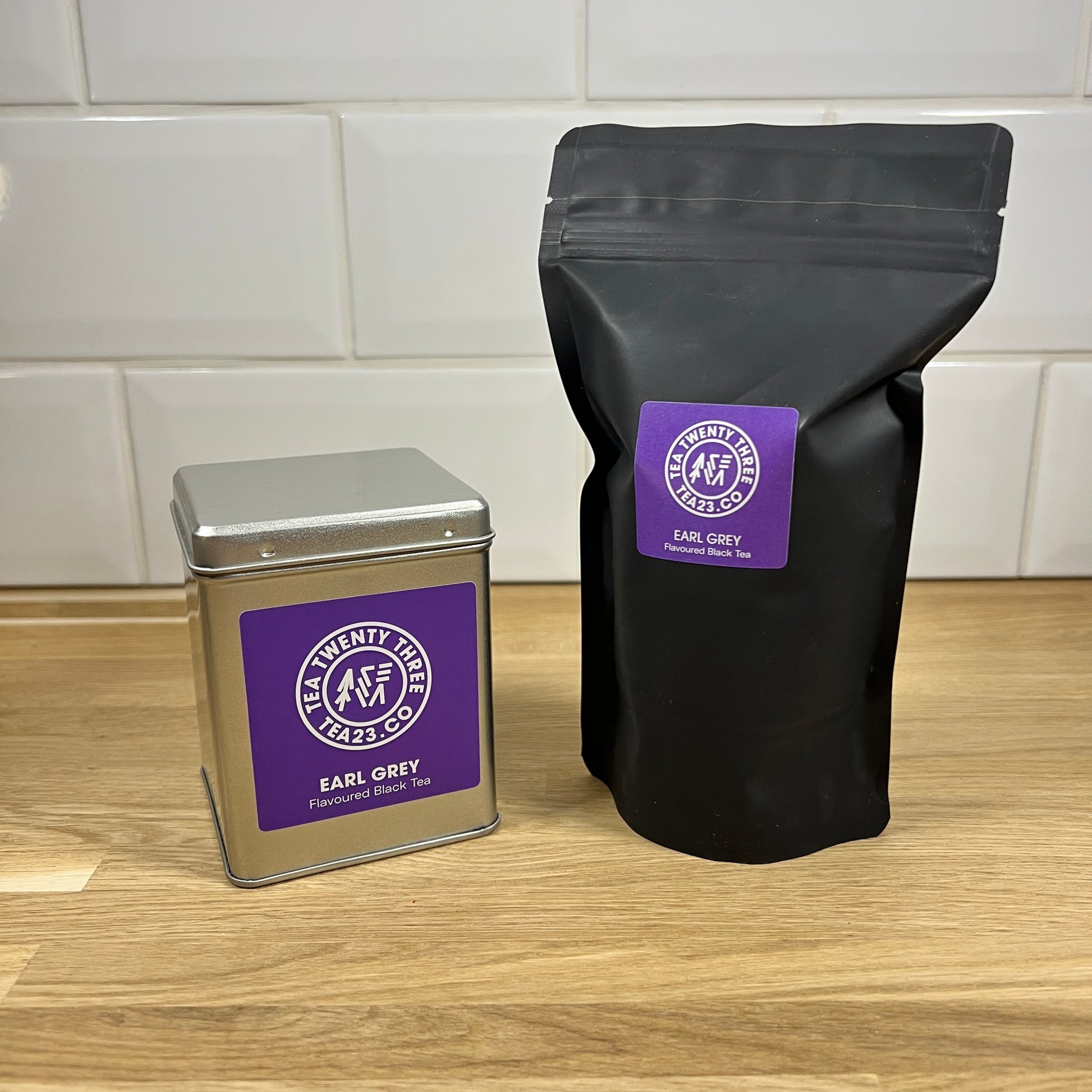 Earl Grey tea packaging including a black bag and silver tin with a purple label on a wooden surface.