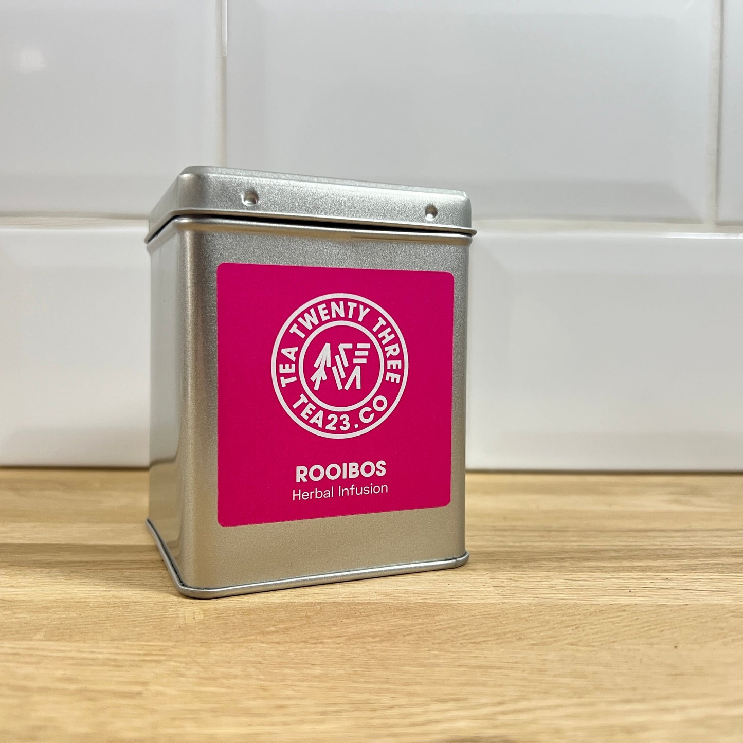 Silver tea tin with a pink label on a wooden surface