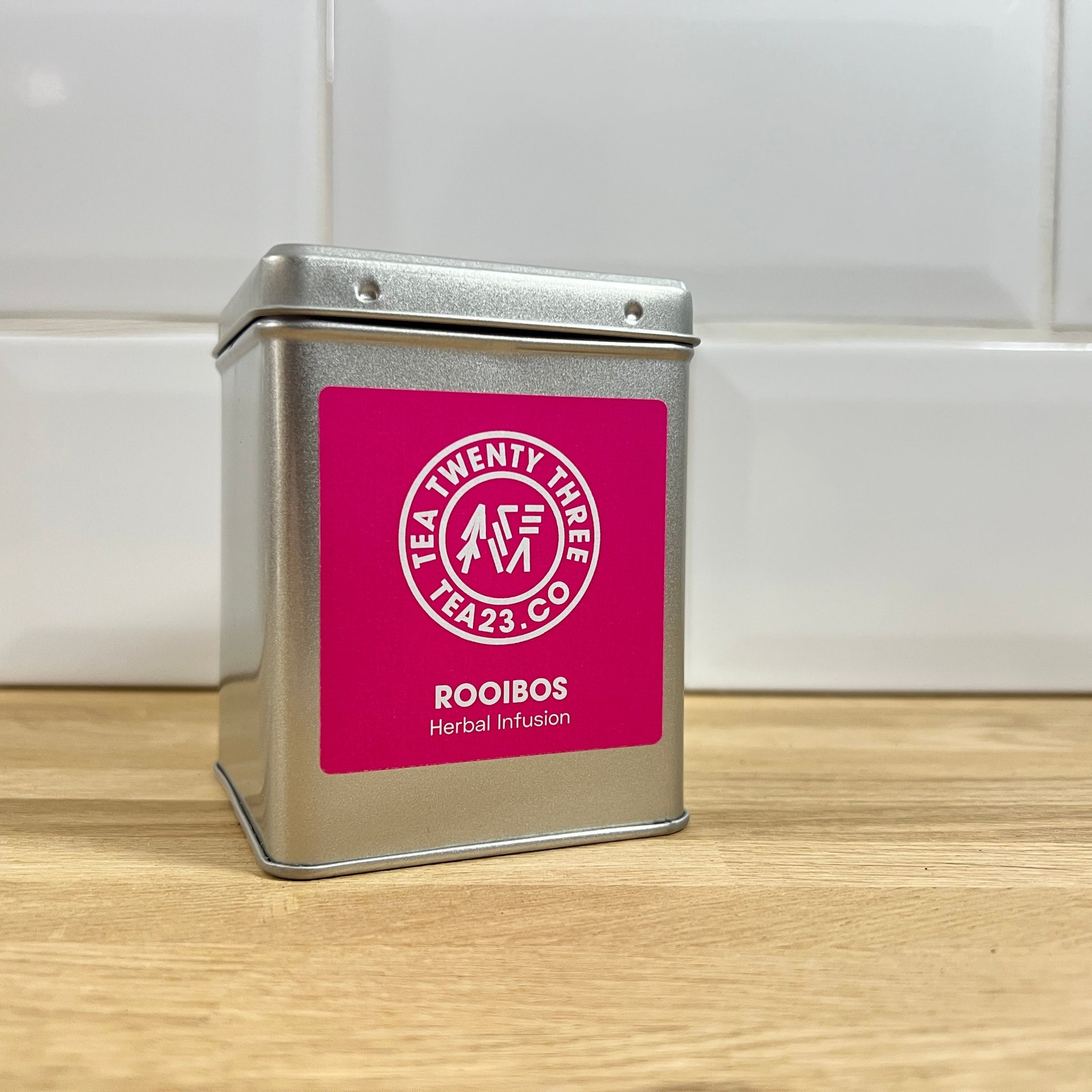 Silver tea tin with a pink label on a wooden surface