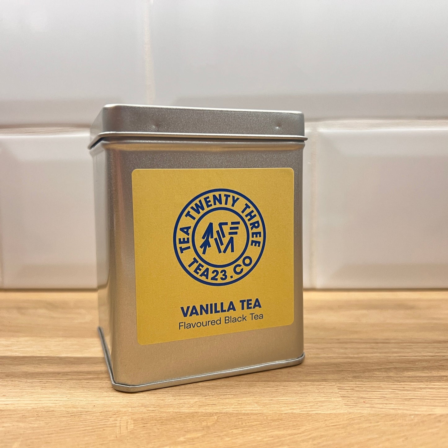 Silver tea canister with a yellow label featuring 'Tea Twenty Three' branding on a wooden surface.