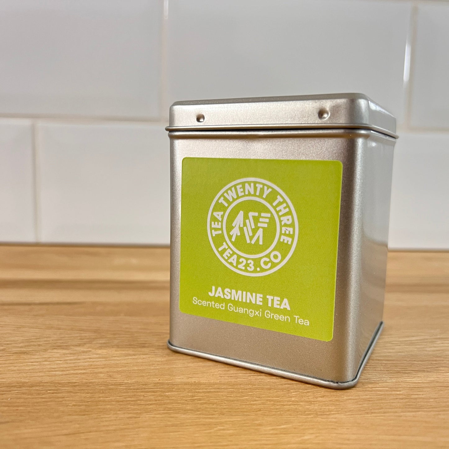 Silver tea canister of Jasmine Green Tea with a green label on a wooden surface