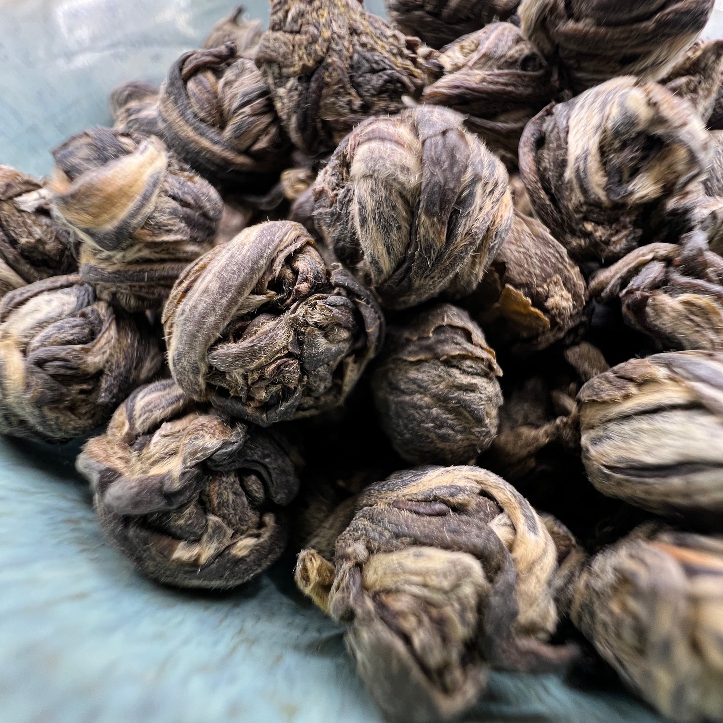A close up of Jasmine Pearls green tea in a blue dish