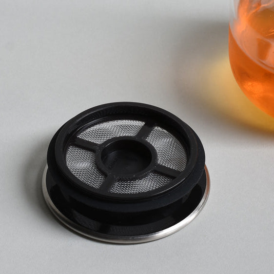 Stainless steel lid with built in tea filter on a table
