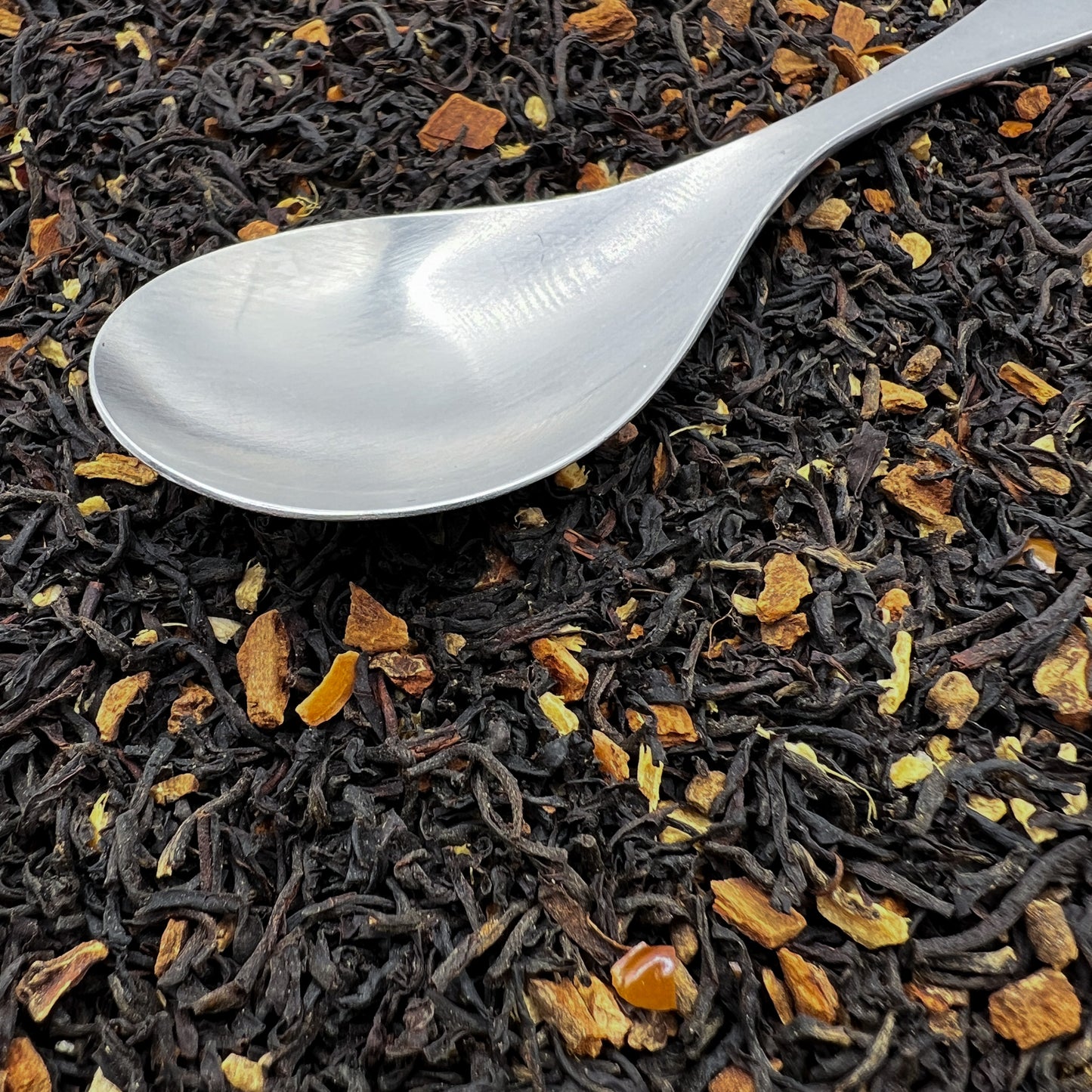 Silver spoon on a bed of black tea leaves with spices