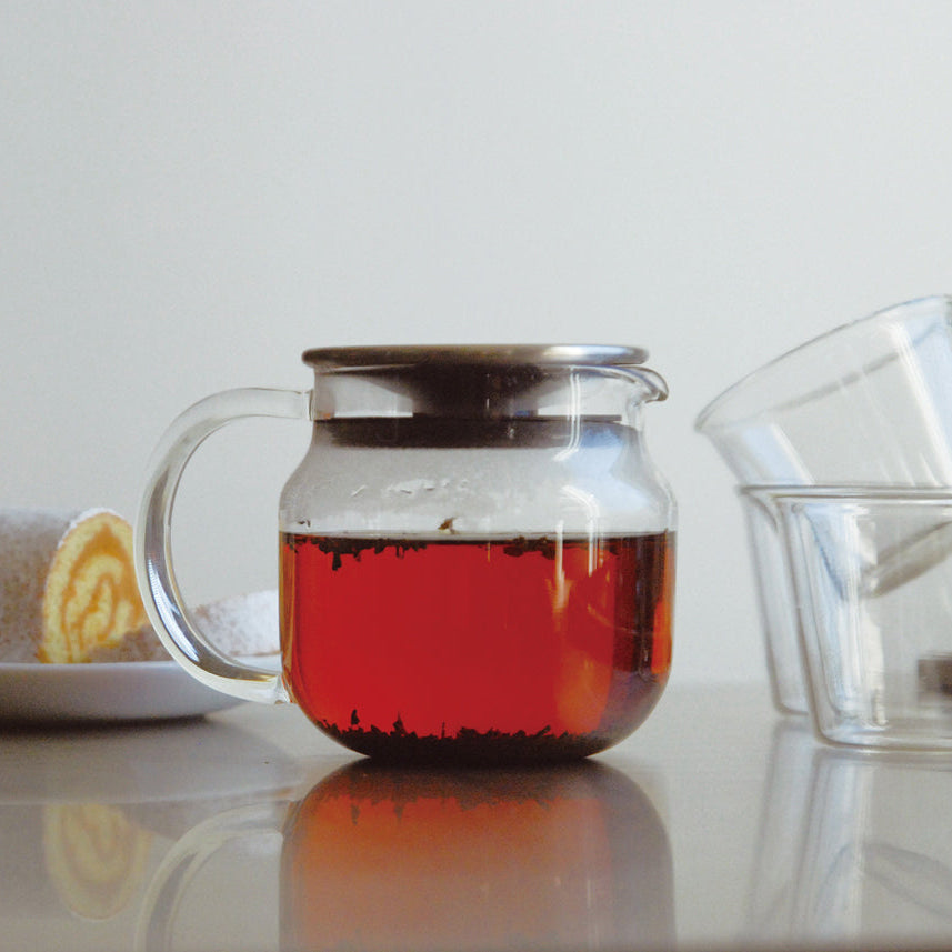 Glass teapot with red liquid on a white surface