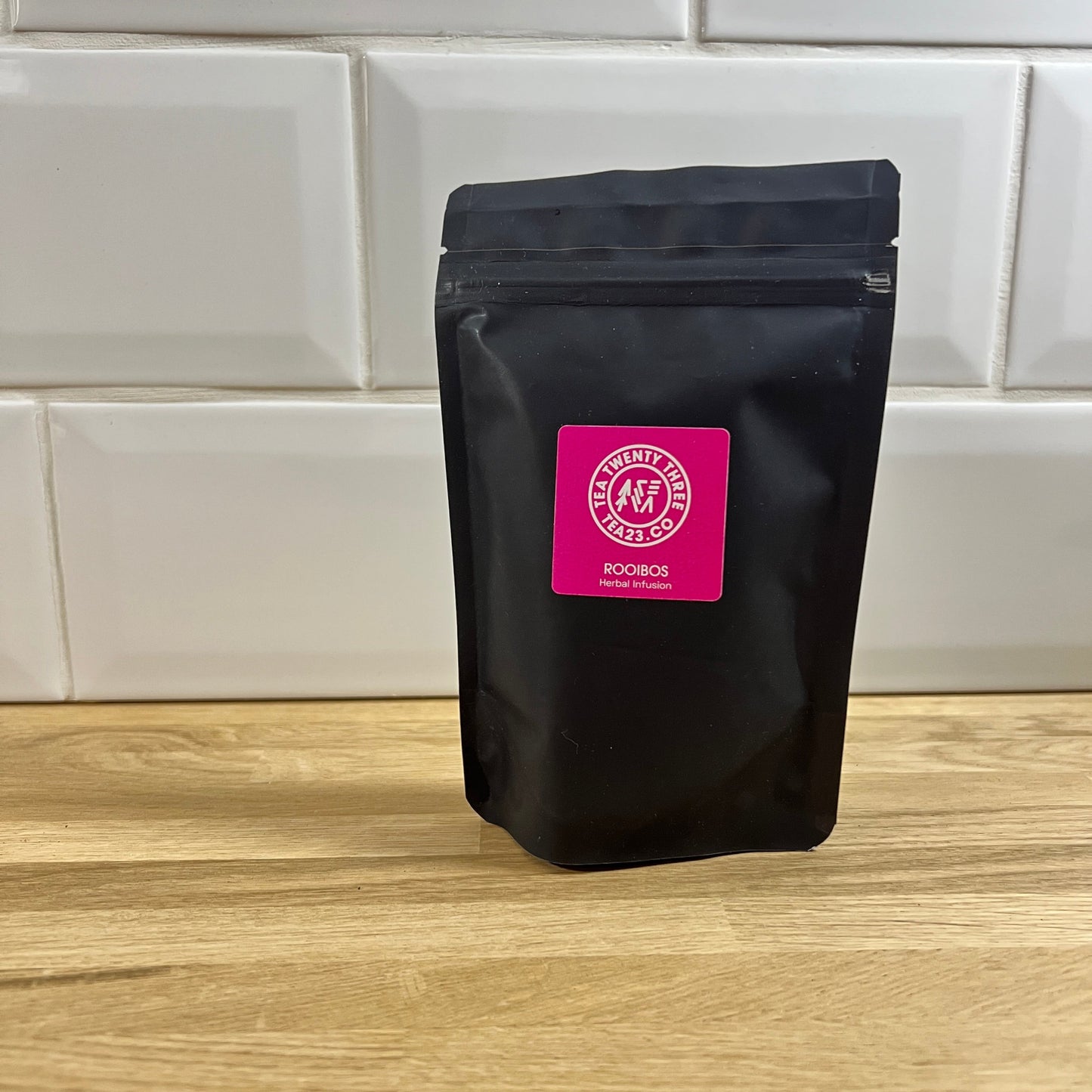 Small black pouch of Rooibos tea with a pink label on a table