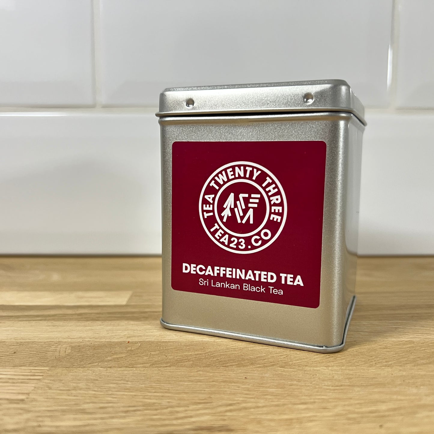 Silver tea canister with burgundy label on a wooden surface