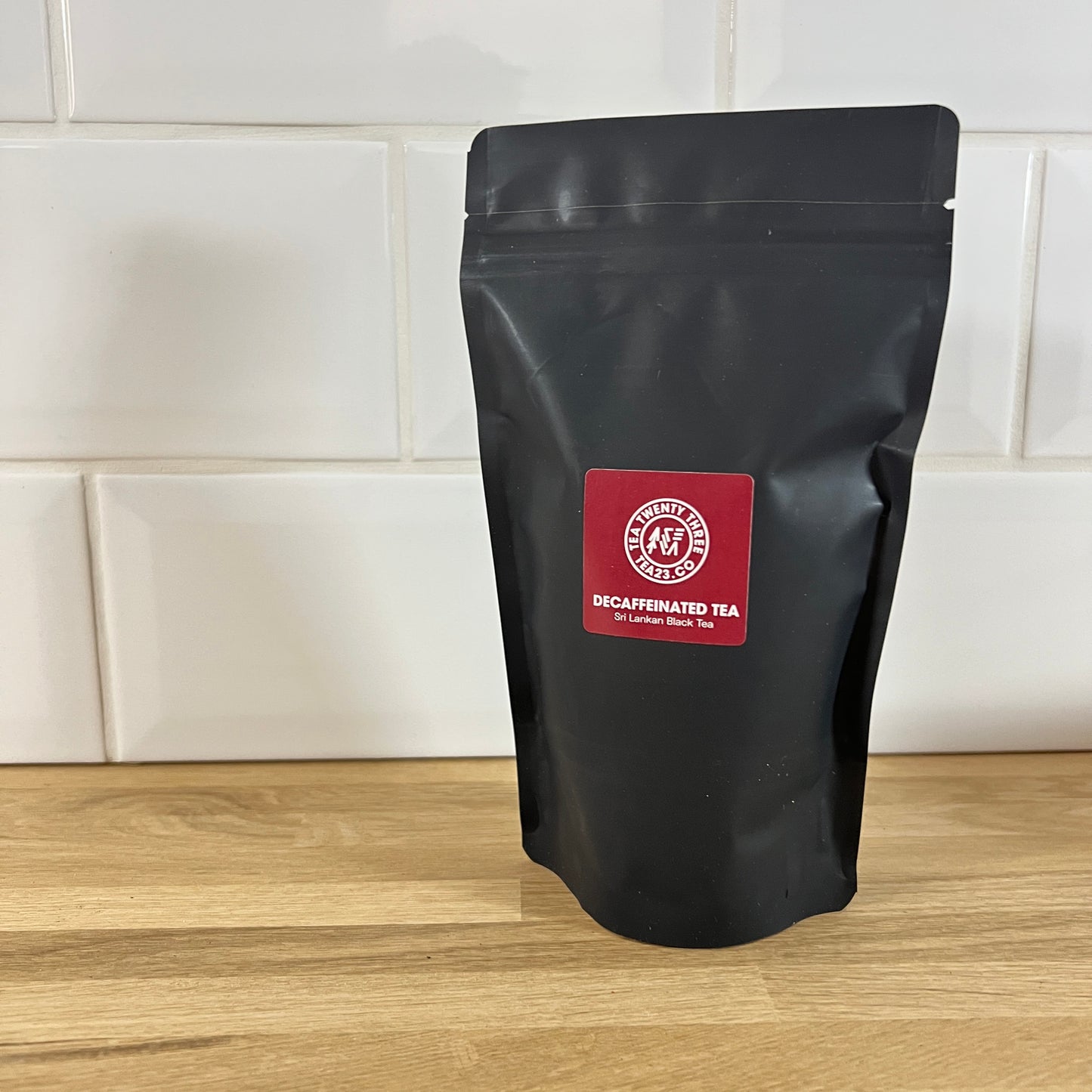 Black tea bag with a burgundy label on a wooden surface with a white tiled wall background