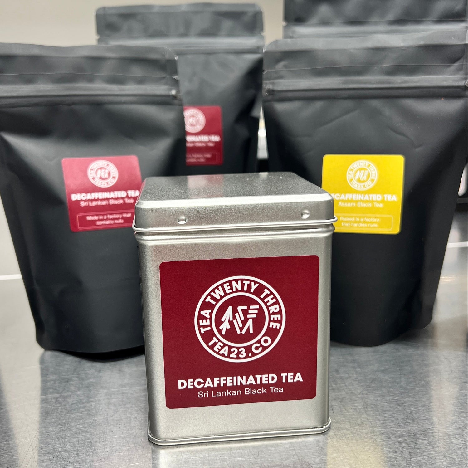 Silver tea canister with red label in front of black tea packages on a reflective surface