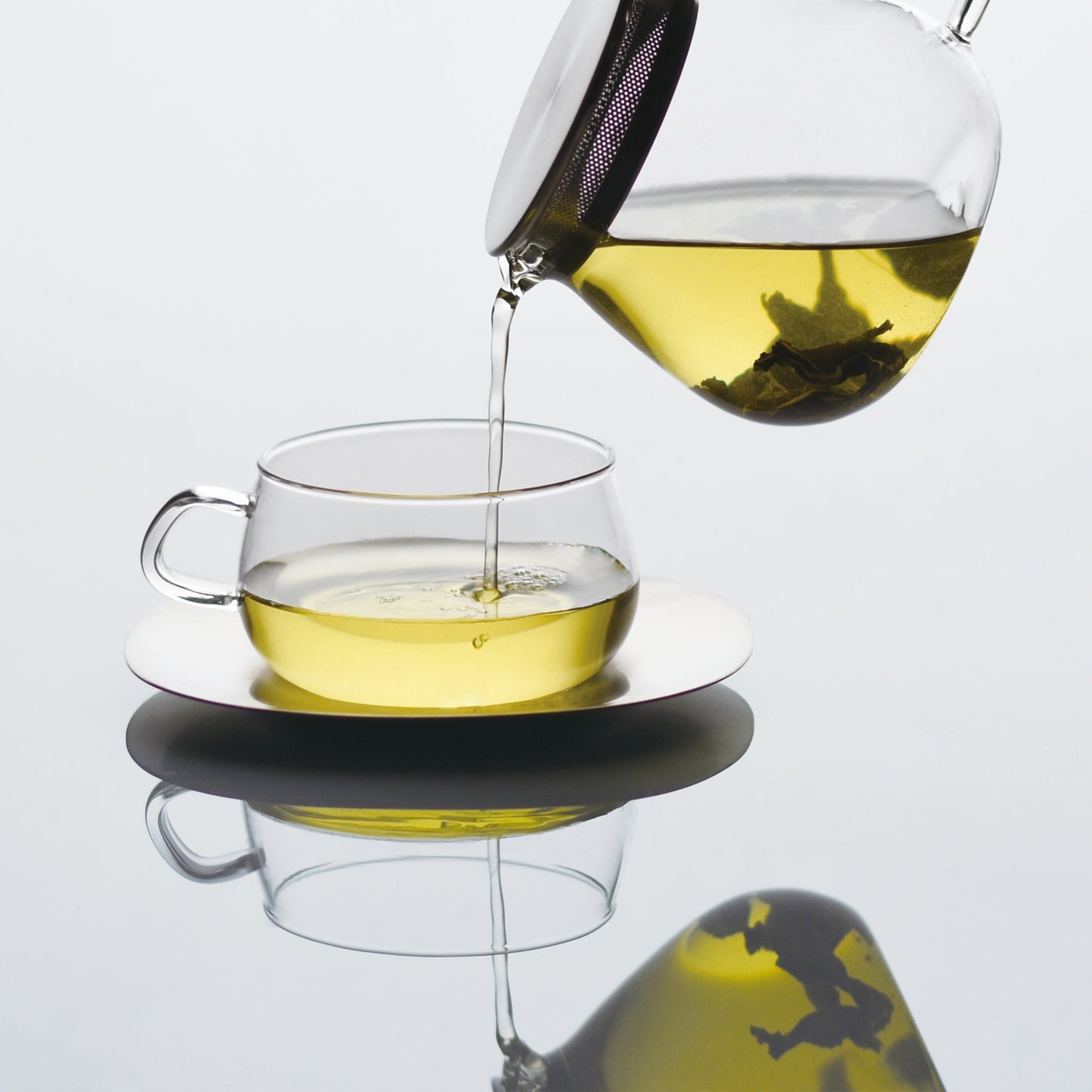 Pouring tea from a glass teapot into a glass cup and saucer
