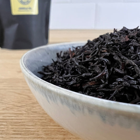 White bowl filled with black tea leaves infused with vanilla on a wooden surface