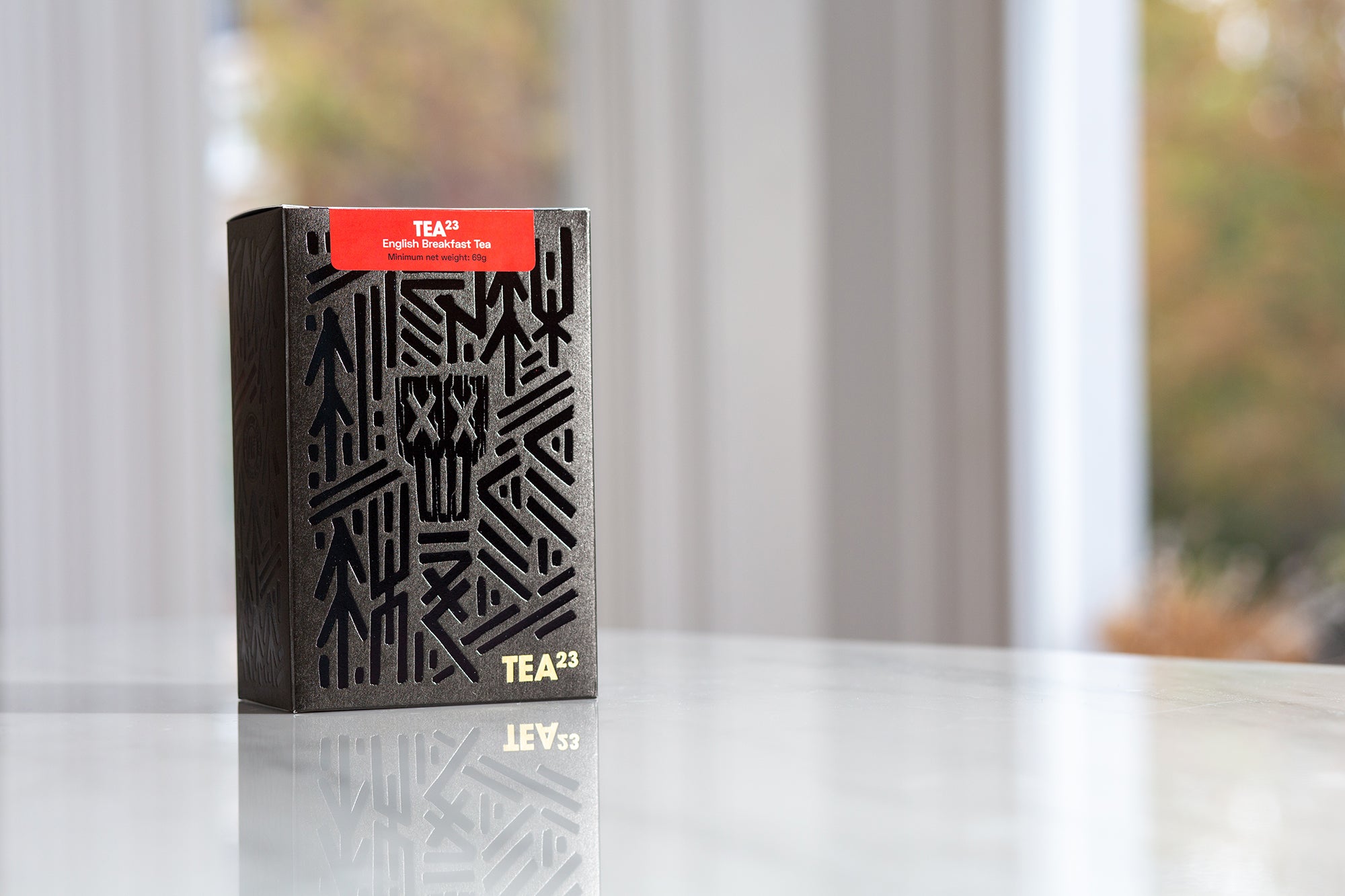 A box of English Breakfast Tea pyramid tea bags from TEA23 sits on a marble kitchen counter top with views of a garden through the window