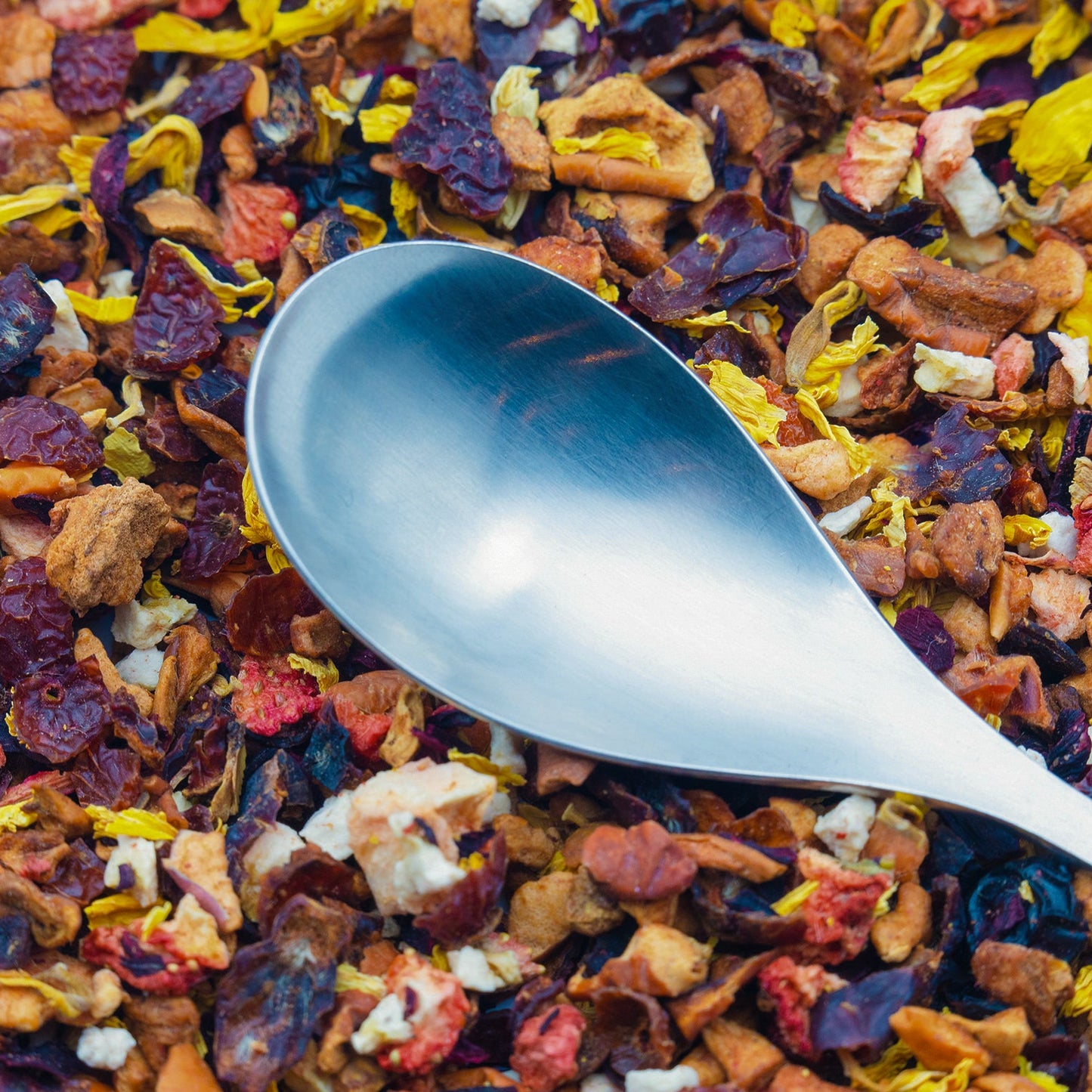 A silver spoon rests on a pile of Banana Berry loose fruit tea