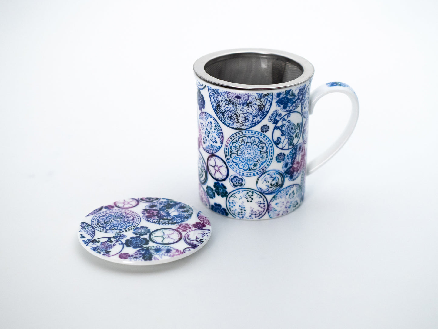 Blue mandala porcelain infuser mug and stainless steel infuser basket stand next its porcelain lid