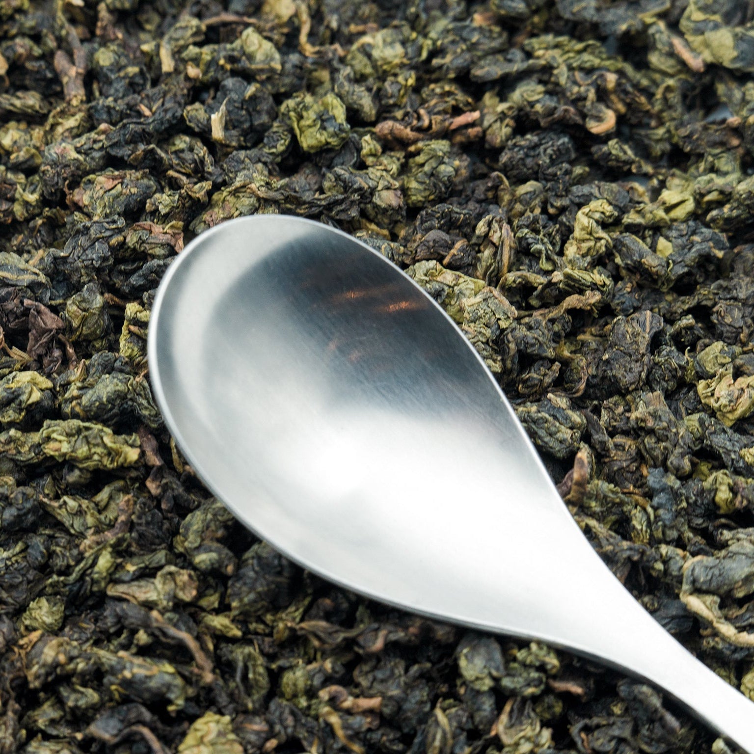 Jade Oolong loose leaf tea with a silver spoon resting on top
