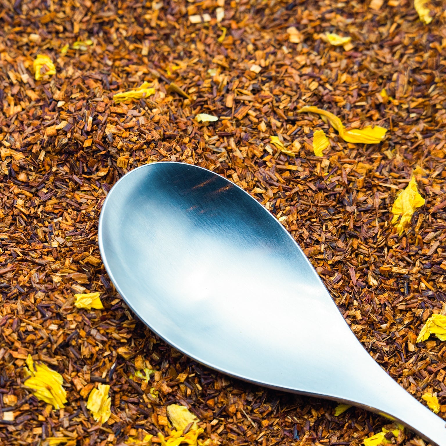 Red Bush tea leaves with a silver spoon on top