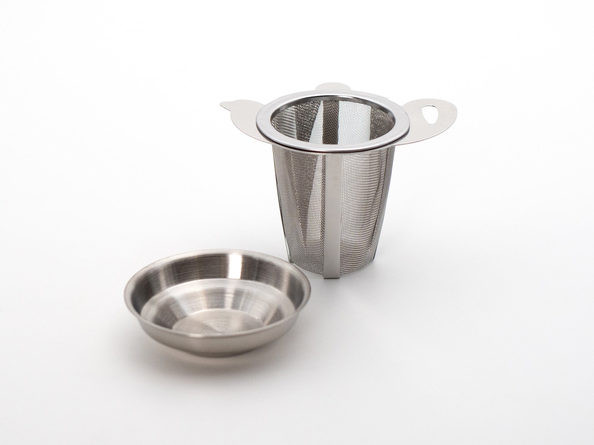 Tea pot shaped stainless steel tea infuser basket next to its stainless steel drip tray