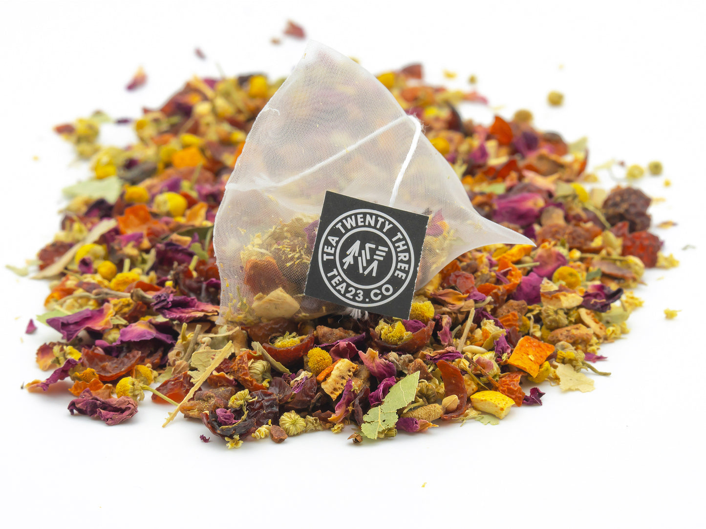 A Chamomile and Pear pyramid tea bag from Tea23 sits on a pile of loose Chamomile and Pear fruit tea