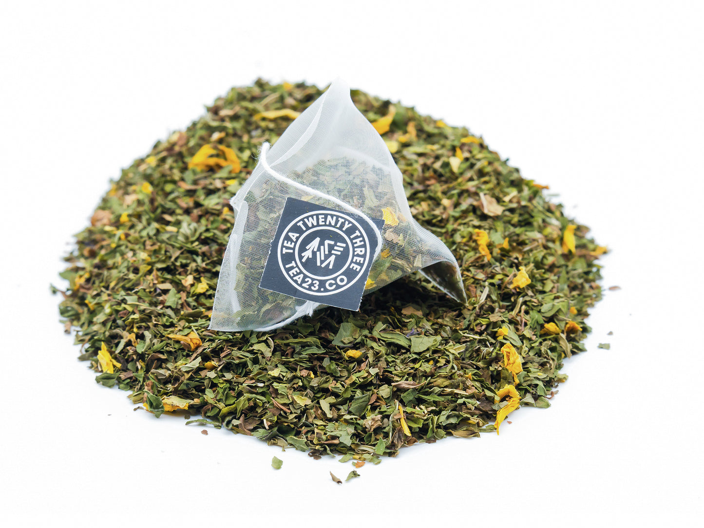A Mint Tea pyramid tea bag from TEA23 sits on a pile of mint tea
