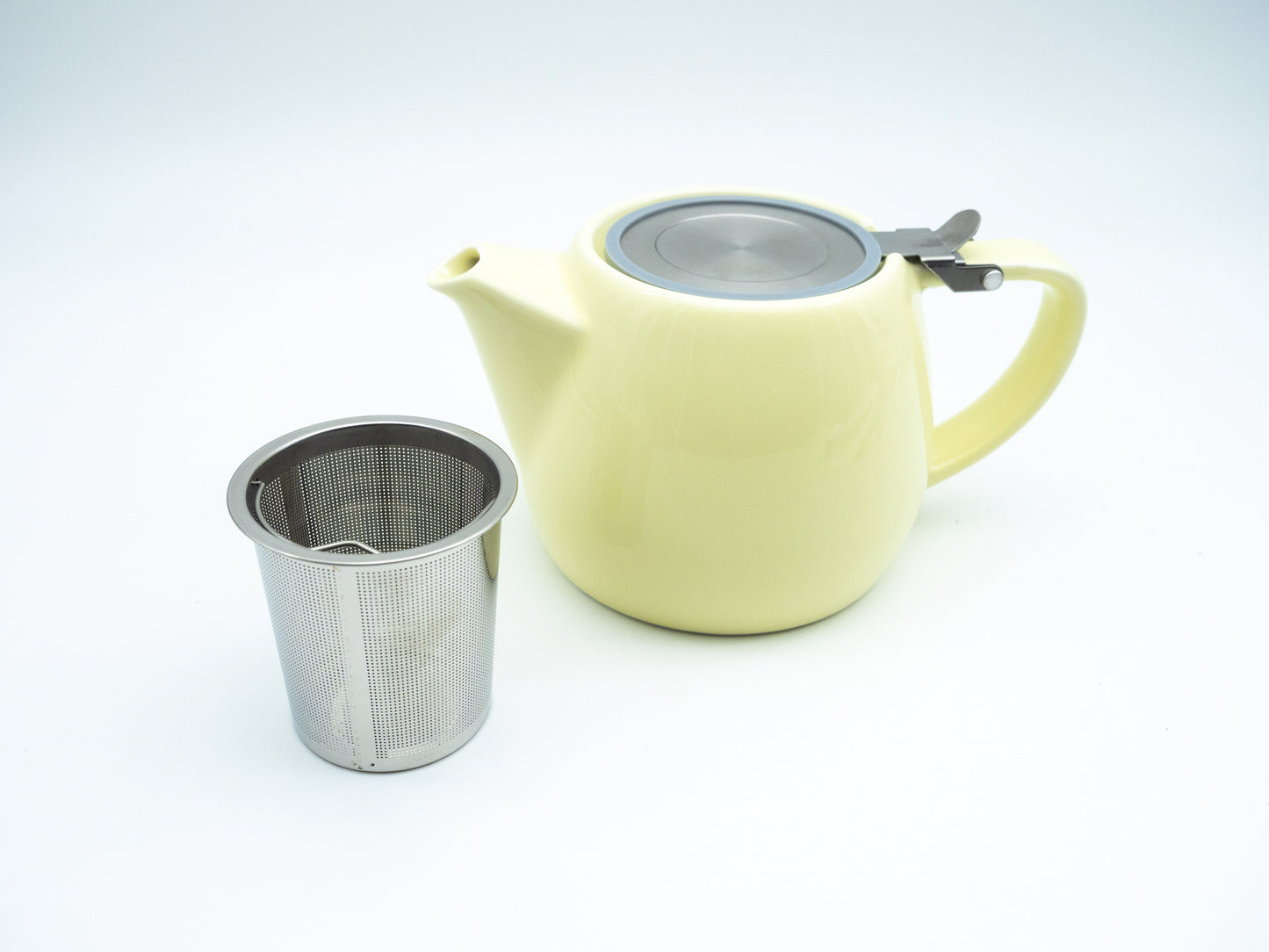 Vanilla porcelain tea pot next to a stainless steel infuser basket