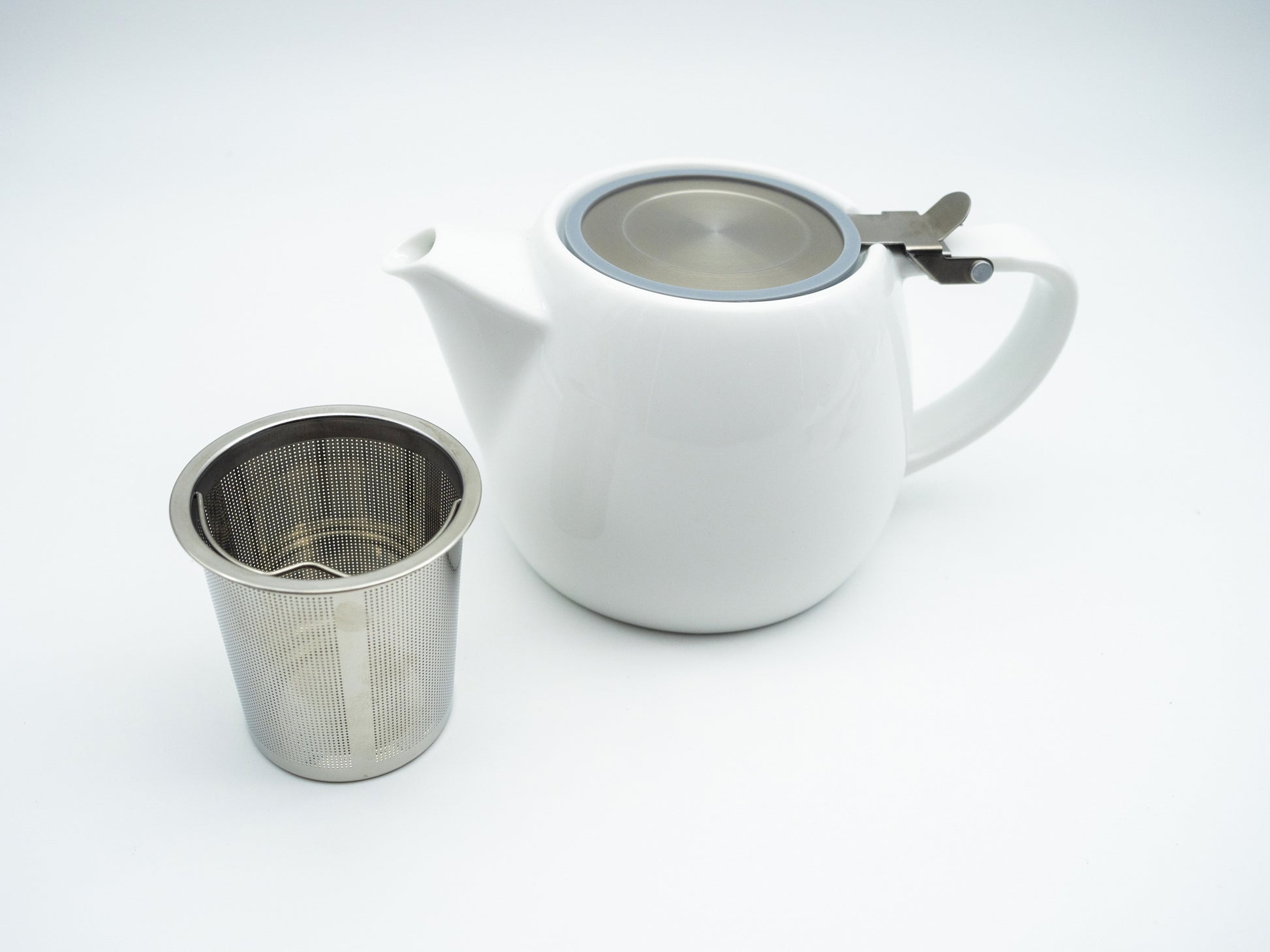 White porcelain stump tea pot next to a stainless steel infuser basket